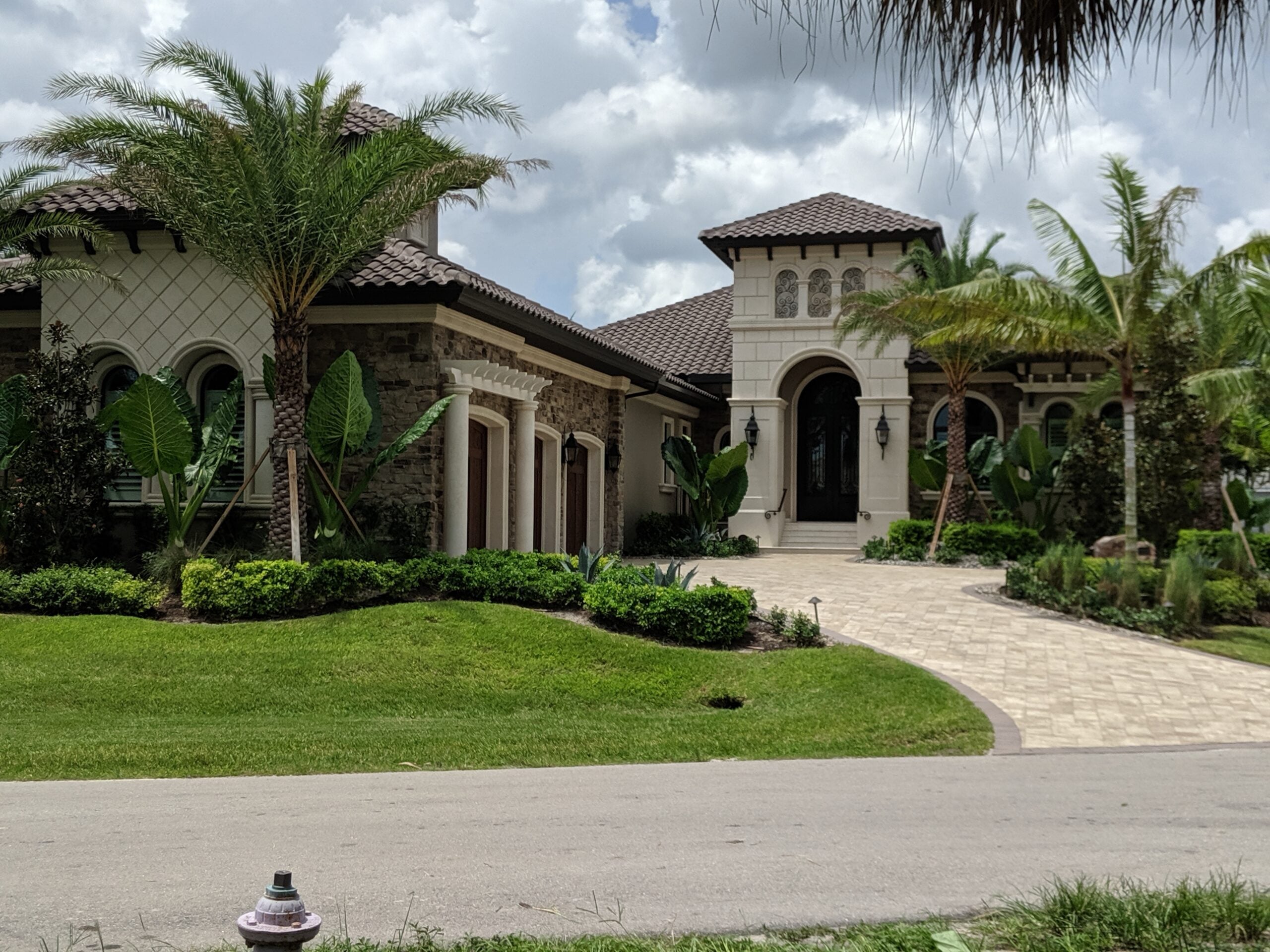 Mediterranean estate with stone columns, arched openings, and palm landscaping